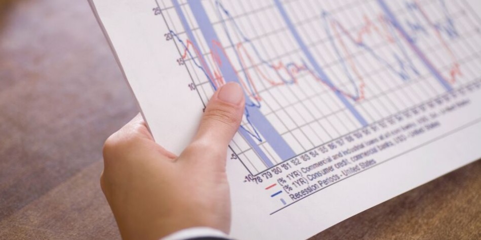 Hand holding paper showing economic indicators